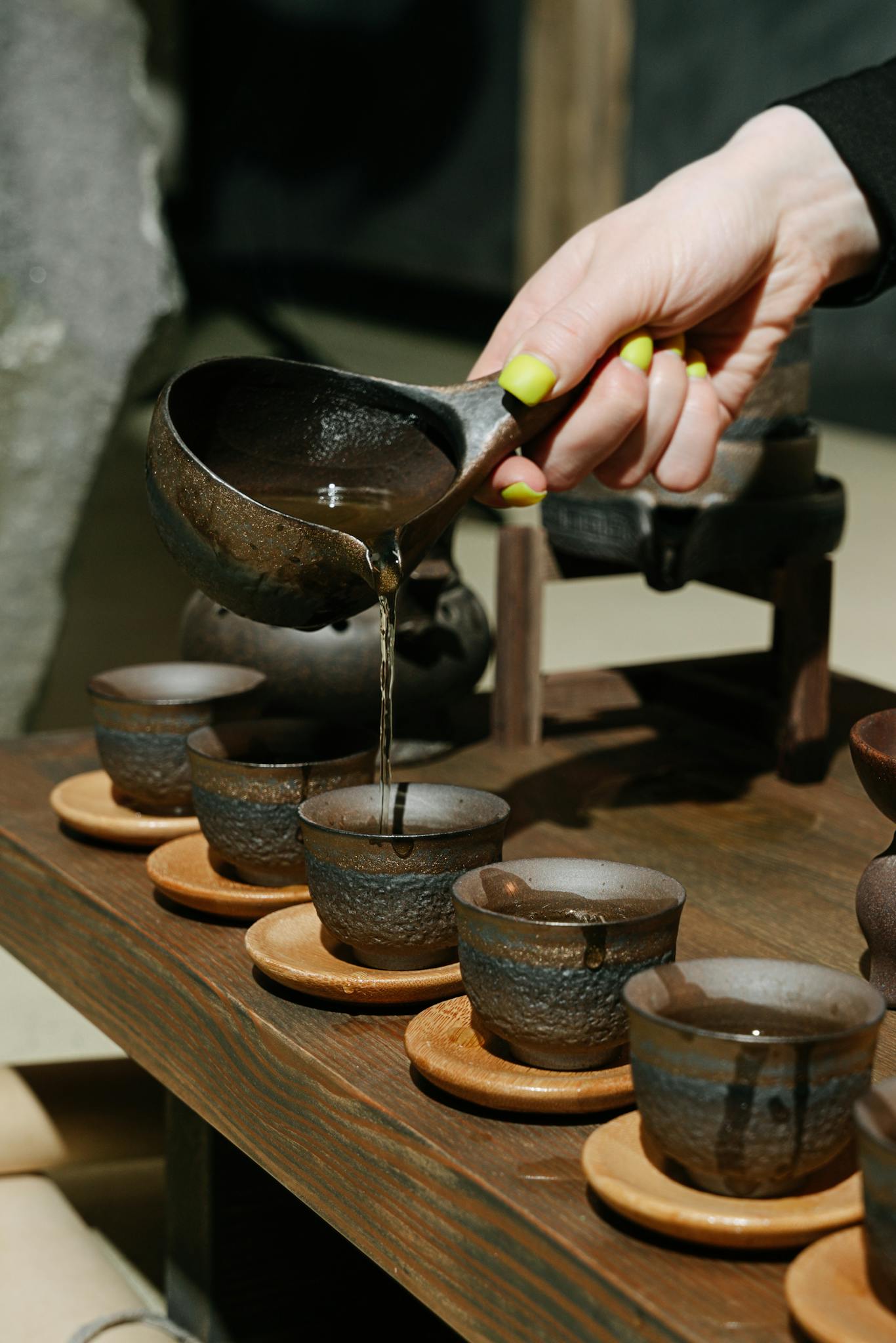 Services服務 Close-up of a hand pouring tea into clay cups, showcasing traditional pottery and tea culture.